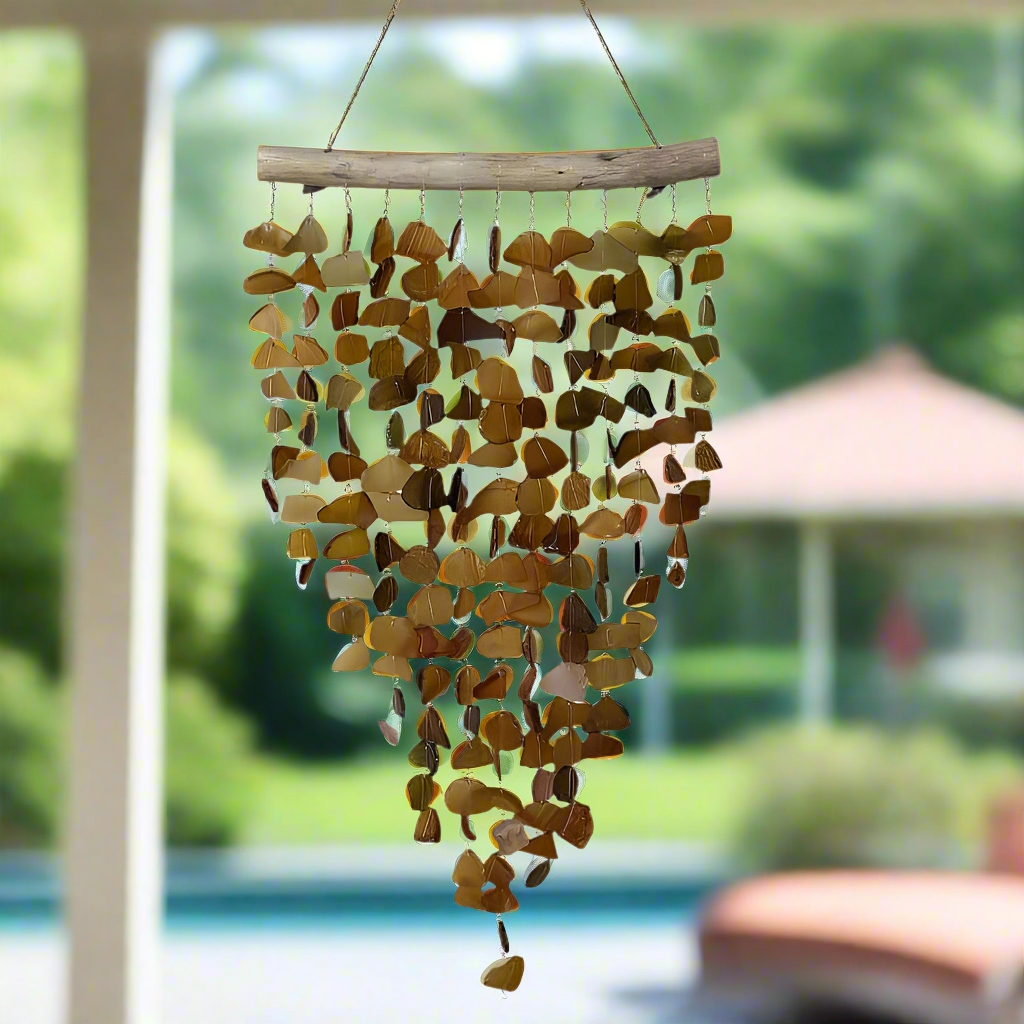A seaglass and driftwood chime hanging in the air, with wooden rope-like strings and various shaped glass pieces, displayed in an outdoor setting.
