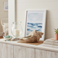 Nautical-themed decor on a wooden console table with a candle, shell, and framed artwork.