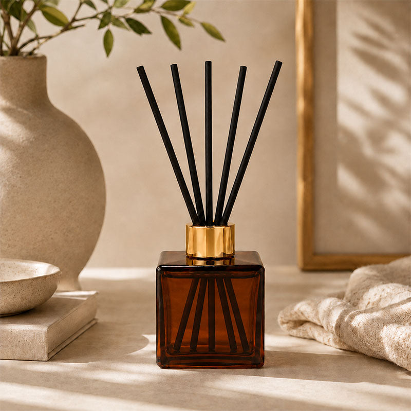 Kairo Reed diffuser with black sticks in amber glass on a surface with decorative items.