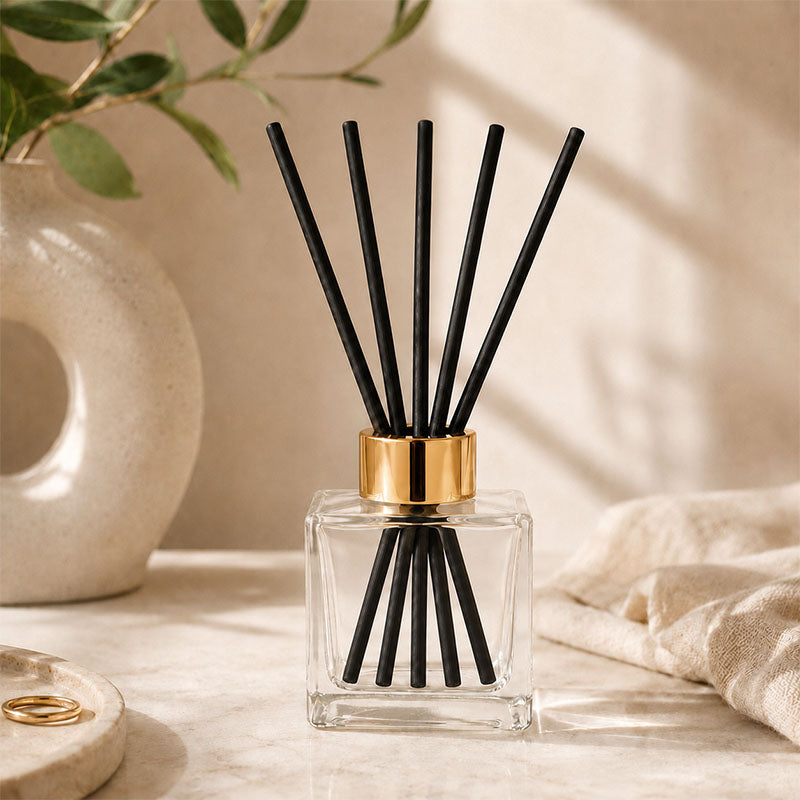 Kairo Reed diffuser with black sticks in a clear square container with gold cap 