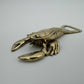 A metallic lobster-shaped bottle opener with a polished gold finish, photographed on a neutral light gray background.