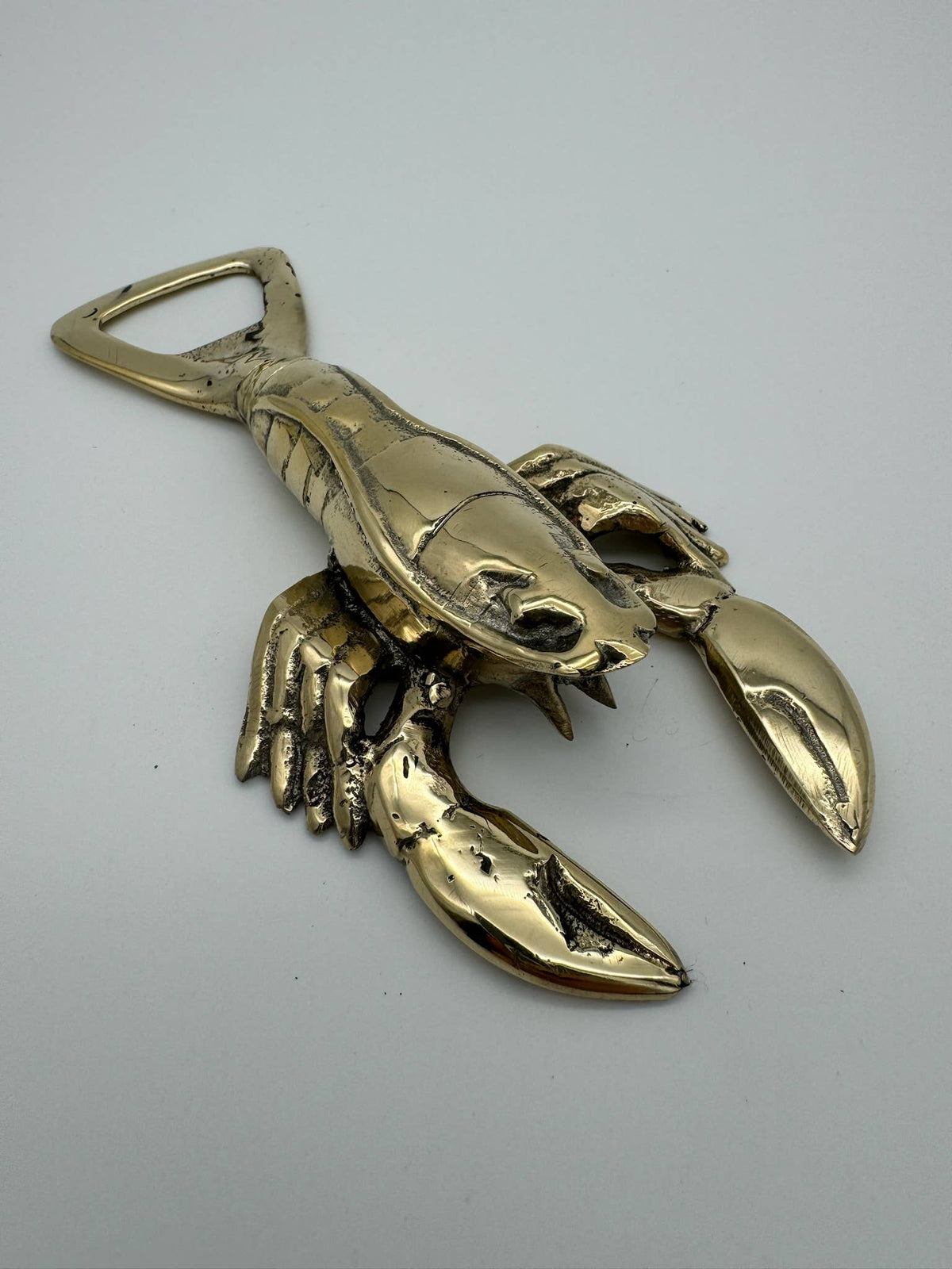 A metallic lobster-shaped bottle opener with a polished gold finish, photographed on a plain light gray background.