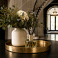 Decorative setup with a vase, flowers, and luxury ayrai diffuser on a gold tray in a home setting.