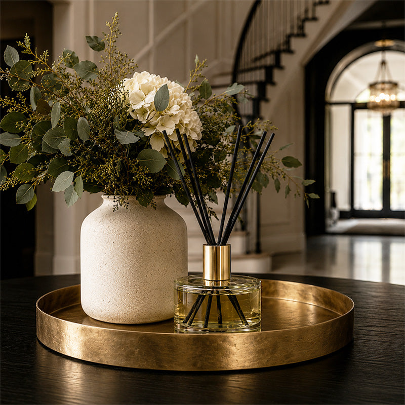Decorative setup with a vase, flowers, and luxury ayrai diffuser on a gold tray in a home setting.