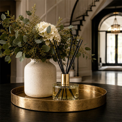 Decorative setup with a vase, flowers, and luxury ayrai diffuser on a gold tray in a home setting.