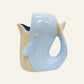 Pale blue ceramic whale jug with cream fins, a curved tail-shaped handle and open top.
