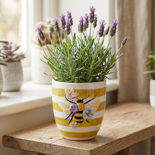 Potted lavender plant in a decorative pot with bee design on a wooden surface.