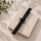 Black diffuser Reed sticks on a light stone surface with green leaves in the corner