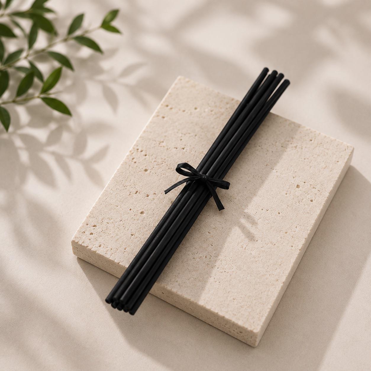 Black diffuser Reed sticks on a light stone surface with green leaves in the corner