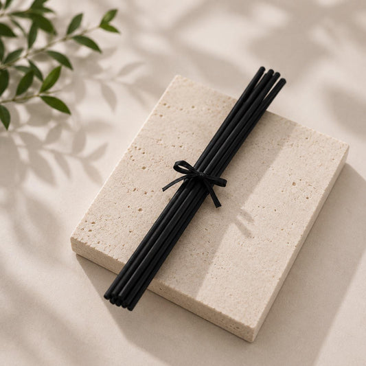 Black diffuser Reed sticks on a light stone surface with green leaves in the corner