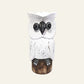 A white owl figurine with black painted details and a distressed finish, perched on a brown wooden 