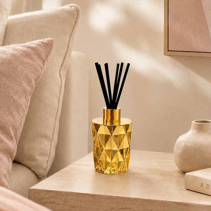 Gold geometric diffuser on a wooden side table with a neutral-colored sofa and decor in the background