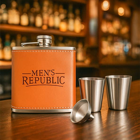 Orange flask with 'Men's Republic' branding on a bar counter with shot glasses and a funnel.