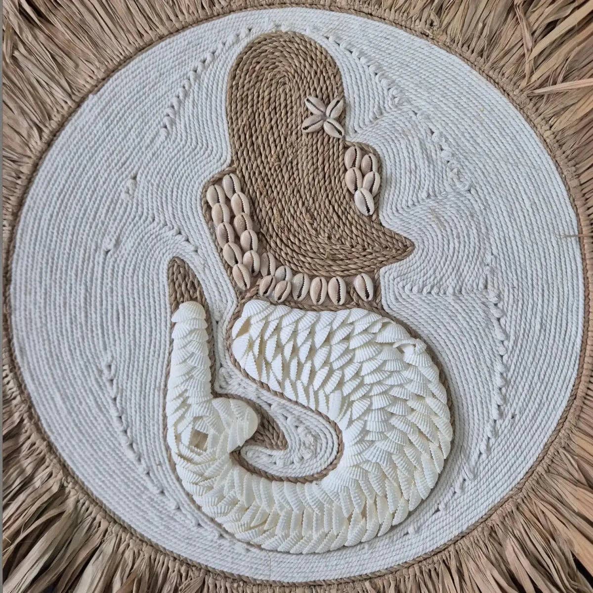 A circular woven wall hanging or rug featuring a stylized mermaid design made from natural jute rope, cowrie shells, and small seashells, set against a circular white woven center and a natural straw border.