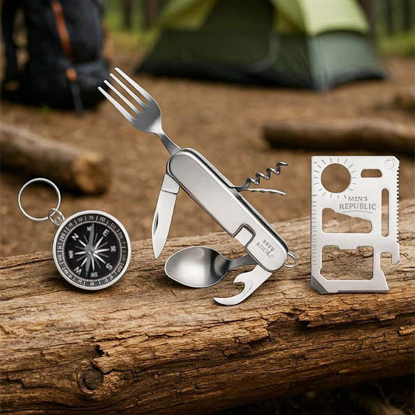 A stainless steel multi-tool pocket knife set displayed on a log in a forest setting, featuring a fork, corkscrew, spoon, and a card tool holder.