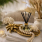 Pjneapply gold tray holding a glass diffuser and a wooden bead garland, ontop of two books next to a cadle and foliage
