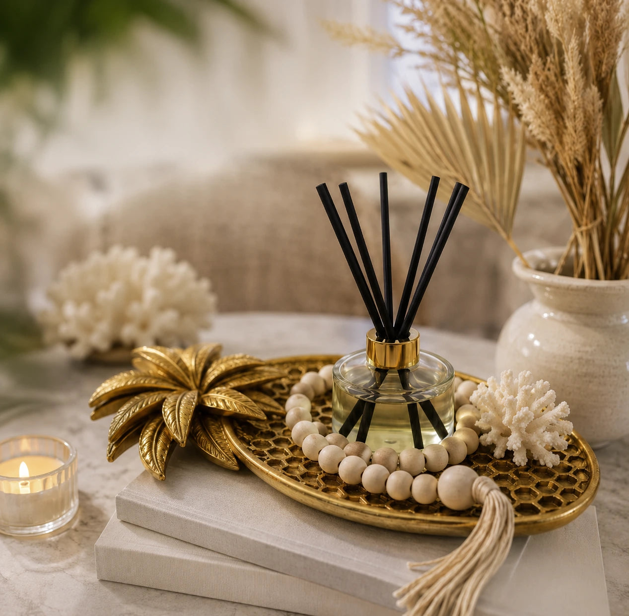 Pjneapply gold tray holding a glass diffuser and a wooden bead garland, ontop of two books next to a cadle and foliage
