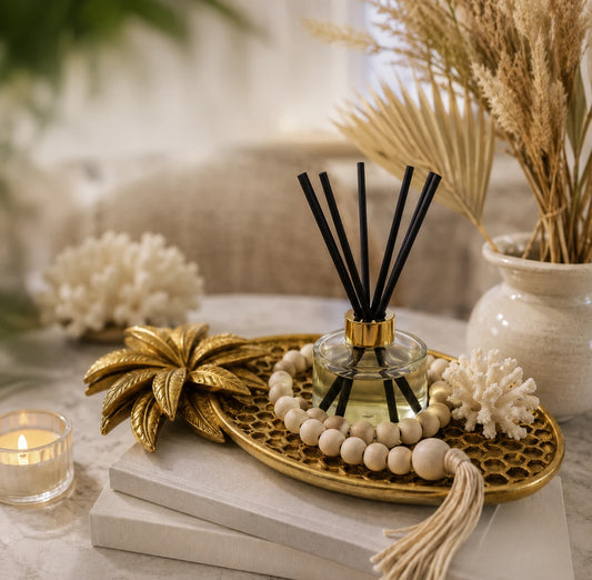 Pjneapply gold tray holding a glass diffuser and a wooden bead garland, ontop of two books next to a cadle and foliage
