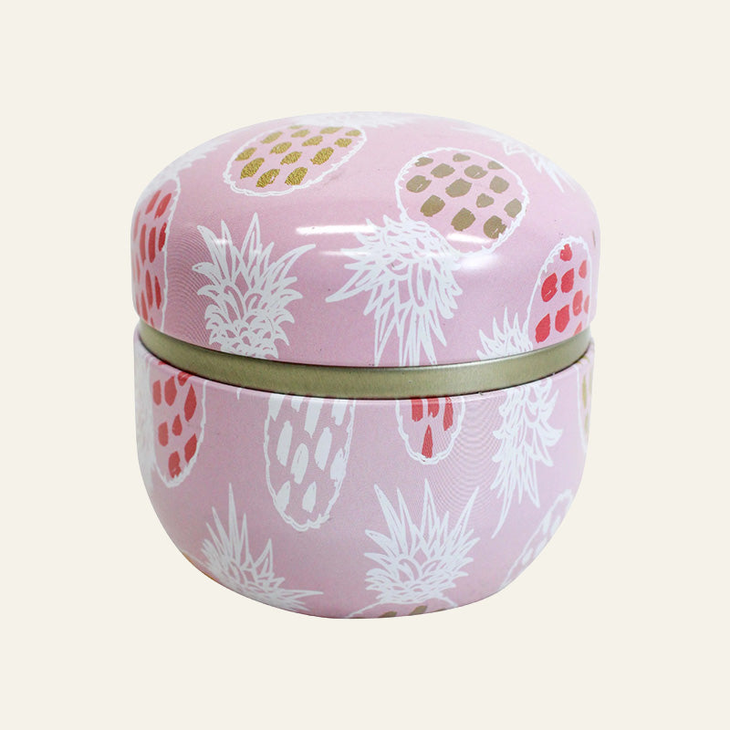 Pastel pink metal trinket tin with white and coloured pineapple print and gold-tone lid.