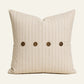 Tan pinstripe French linen cushion cover with four coconut buttons on a warm ivory background.