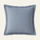 A square throw pillow in a dusty light blue linen fabric with a matching piped border.