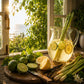 Clear pitcher of lemon water on a wooden surface with lemons and limes, set against a window with greenery outside.