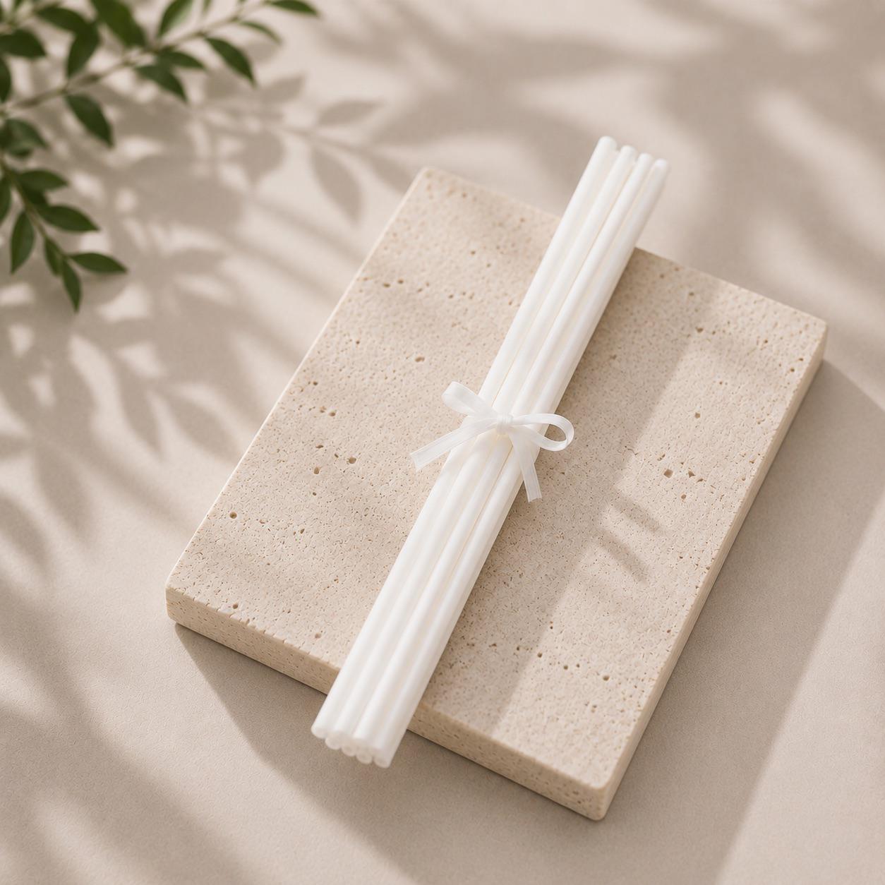 White diffuser Reed sticks on a light stone surface with green leaves in the corner