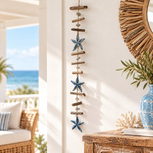 write an ALT text
Coastal driftwood garland featuring three blue starfish, natural wood and stone beads, hanging on a cream wall above a rustic timber console in a beach house interior.