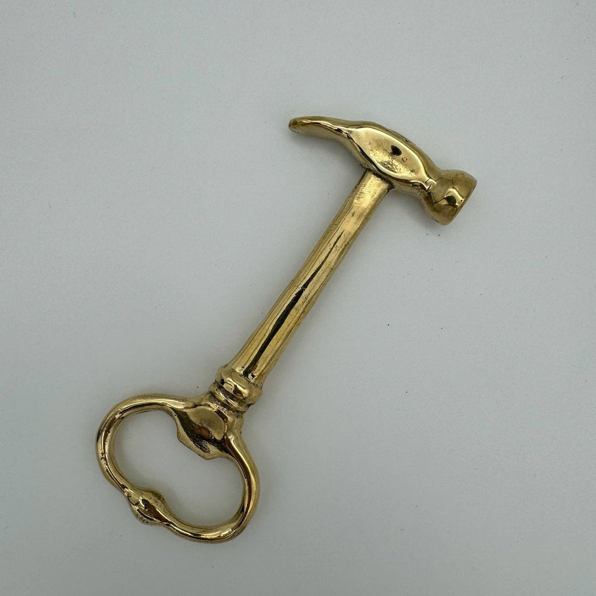 A polished brass hammer-shaped door pull handle with a circular ring knocker, shown on a plain light gray background.