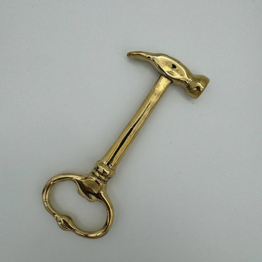 A polished brass hammer-shaped door pull handle with a circular ring knocker, shown on a plain light gray background.