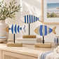 Three decorative fish-shaped wall art pieces with blue and white striped and patterned designs, mounted on black stands with wooden bases, displayed on a light wood console in a styled interior setting.