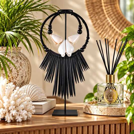 Black circular beaded hoop earrings with white shell-like center accents and long fringe, displayed on a black stand on a wooden table in a styled interior setting with plants and decor.