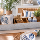 A styled table setting featuring a large woven tray holding blue-and-white lobster-print napkins, gold-toned cutlery, small blue-and-white ceramic shakers, and a small potted green plant, with matching home decor in the background.