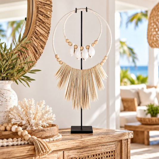 Decorative cuttlefish shell necklace with white shells, natural wooden beads and ivory hanging accents, displayed on a black metal stand atop a timber console in a coastal-style home.