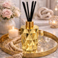 Gold geometric diffuser with black sticks on a decorative tray with candles and flowers.