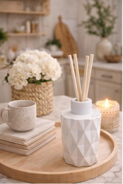 Decorative setting with a mug, diffuser, and flowers on a wooden tray in a kitchen.