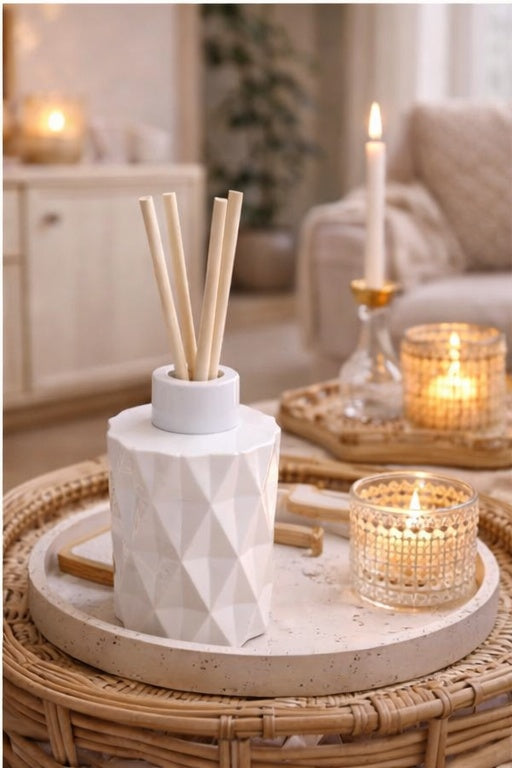 Decorative diffuser with sticks on a wicker table with candles in a cozy room.