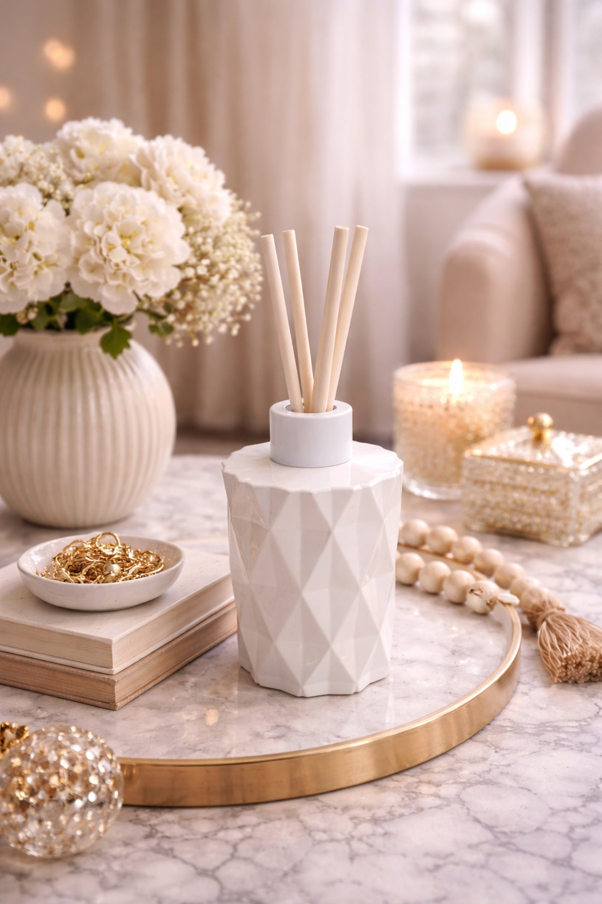 Decorative setup with a geometric vase, flowers, candles, and books on a marble surface.
