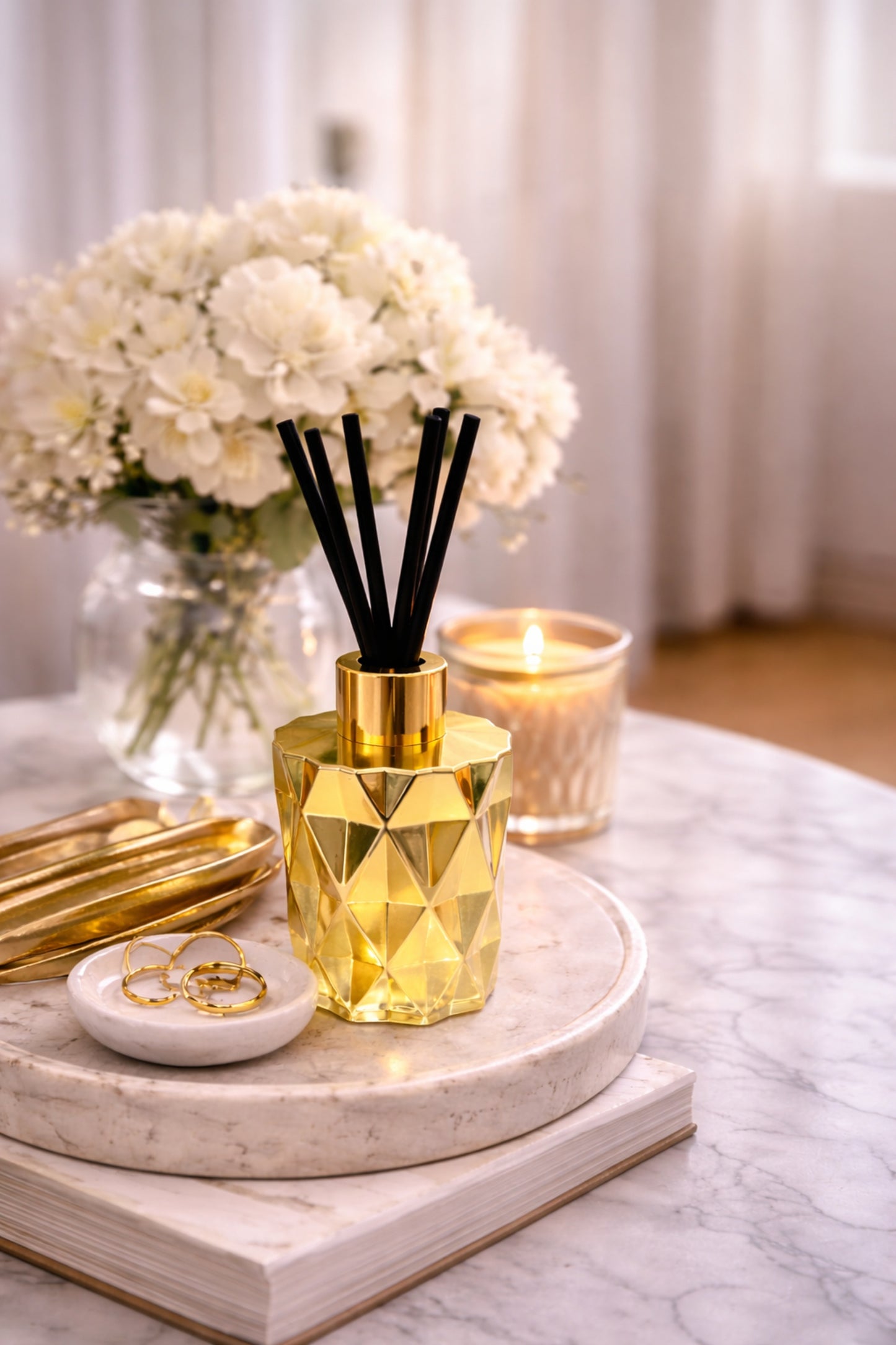 Gold geometric diffuser with black reeds on a marble surface with flowers and a candle in the background.