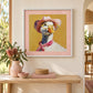 A framed art print featuring a whimsical painting of a duck wearing a pink hat, yellow glasses, and a pink scarf, displayed on a beige wall above a wooden console table with decorative items.