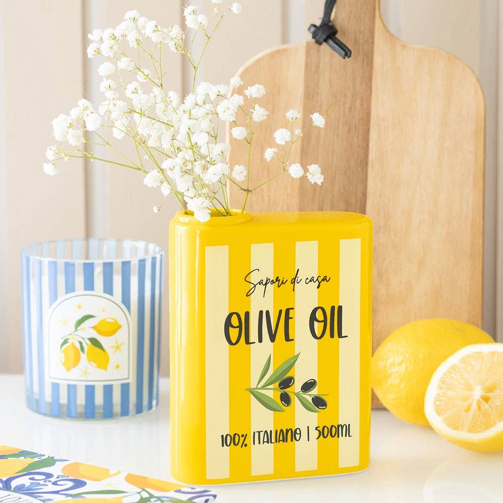 Yellow olive oil container with a striped candle and lemons on a table.