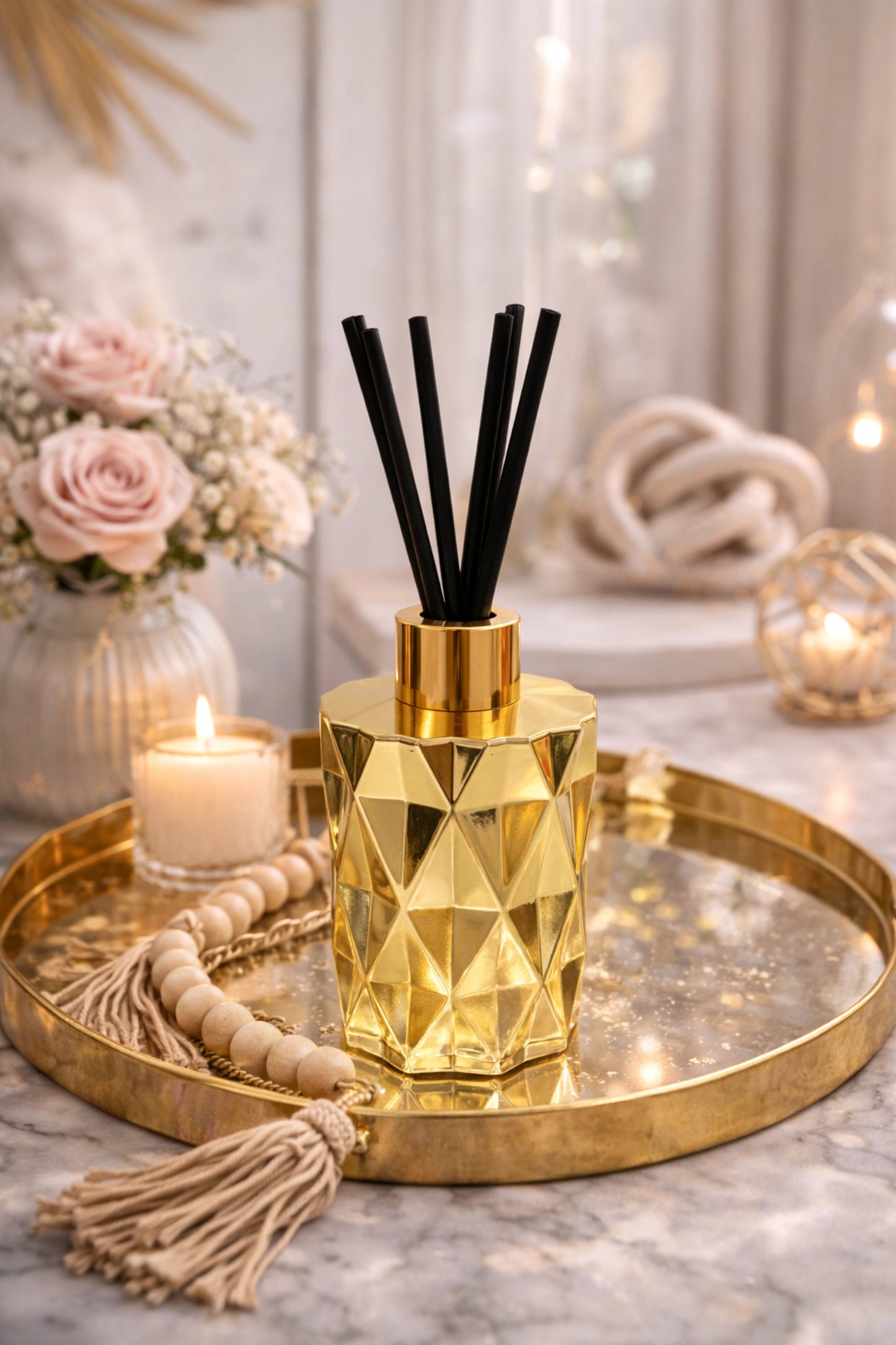 Gold geometric diffuser with black sticks on a decorative tray with candles and flowers.