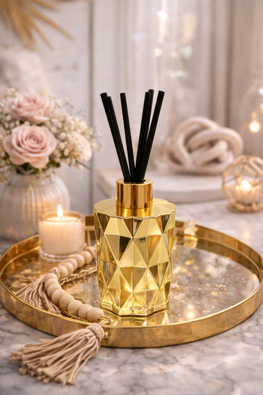 Gold geometric diffuser with black sticks on a decorative tray with candles and flowers.