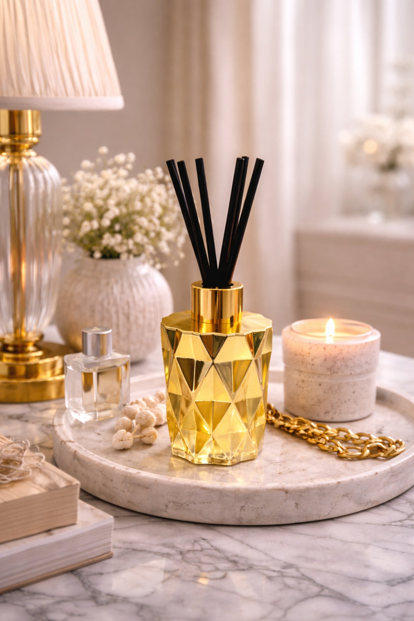 Gold geometric diffuser with black sticks on a marble tray with candles and decor items.
