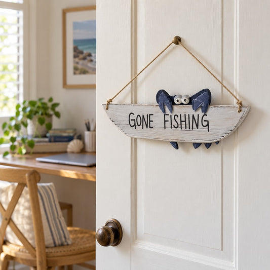 Gone Fishing sign with a navy crab hanging on a white home-office door, with a sunlit desk behind.