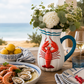 Table setting with a lobster-themed pitcher, lemons, oysters, and shrimp.