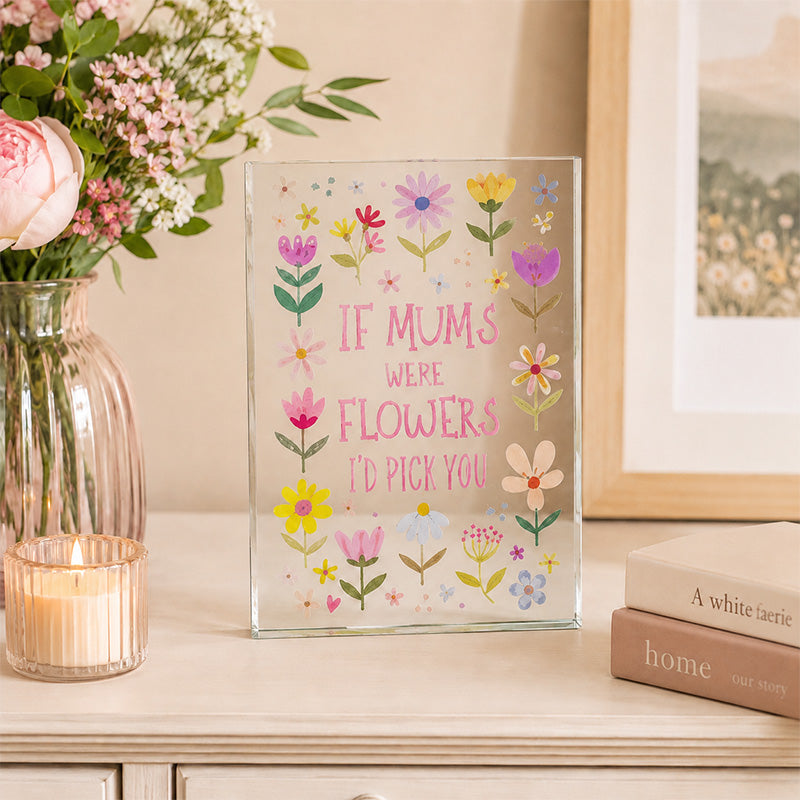 Decorative glass panel with floral design and text on a table with flowers and books.