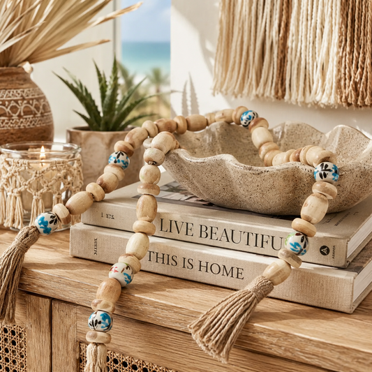 Decorative beaded garland with tassels on a wooden surface with books and plants in the background.