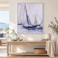 A framed watercolor painting of sailboats in a light blue and white sea, displayed on a beige wall above a rustic wooden console table decorated with a glass vase, driftwood, books, and a woven basket.