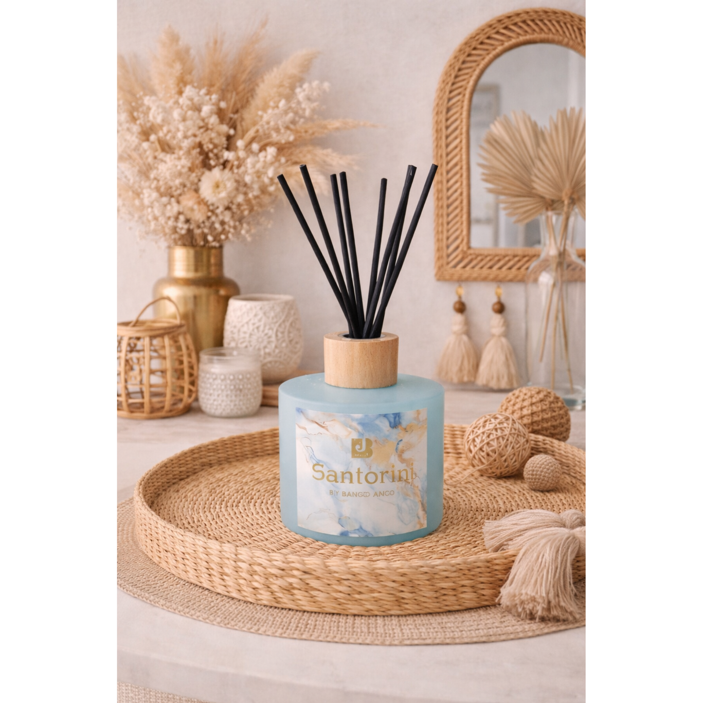 Scented candle with diffuser sticks on a decorative table with dried plants and a mirror.